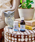 Herbion Memory Support Capsules and Liquid placed on a table along with books and a plant. 